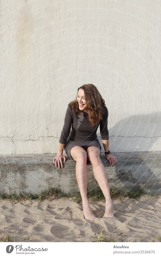 Portrait of a young woman in front of a concrete wall on the beach Woman girl already Slim brunette Curl long hairs Evening Beauty and beauty portrait