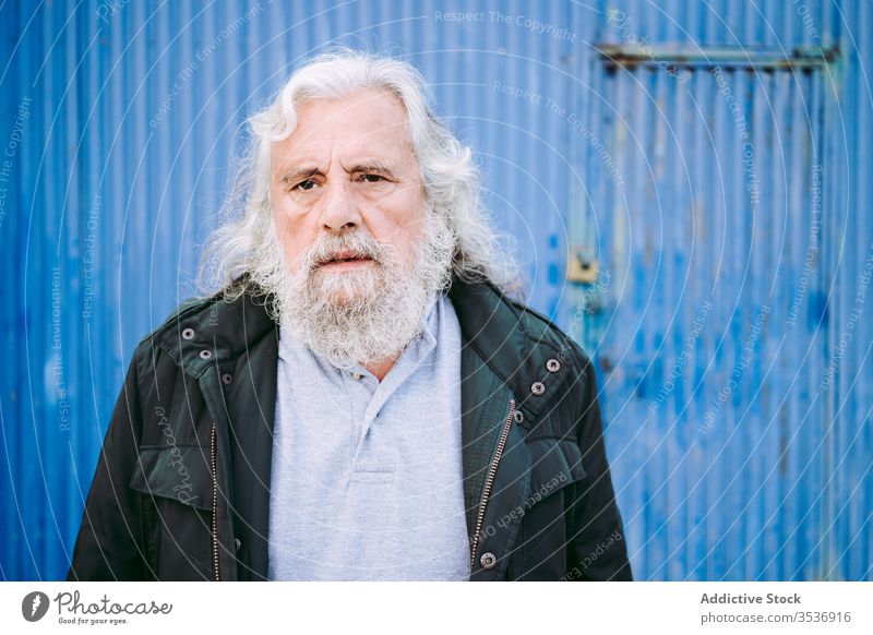 Wrinkled old man slapping face with palm against blue wall wrinkle garage lifestyle signet pensive elderly shabby senior aged thoughtful serious rub male jacket