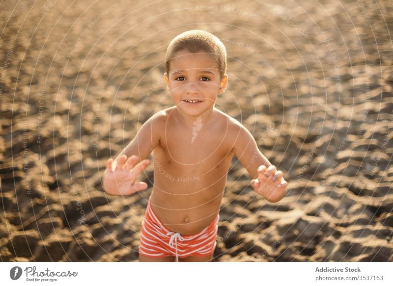 Cheerful boy on beach in evening sea sunset smile resort shirtless summer vacation relax kid lifestyle rest sand cheerful shore joy coast happy glad sundown