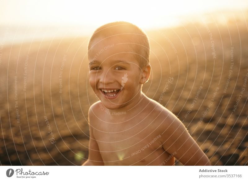 Cheerful boy on beach in evening sea sunset smile resort shirtless summer vacation relax kid lifestyle rest sand cheerful shore joy coast happy glad sundown