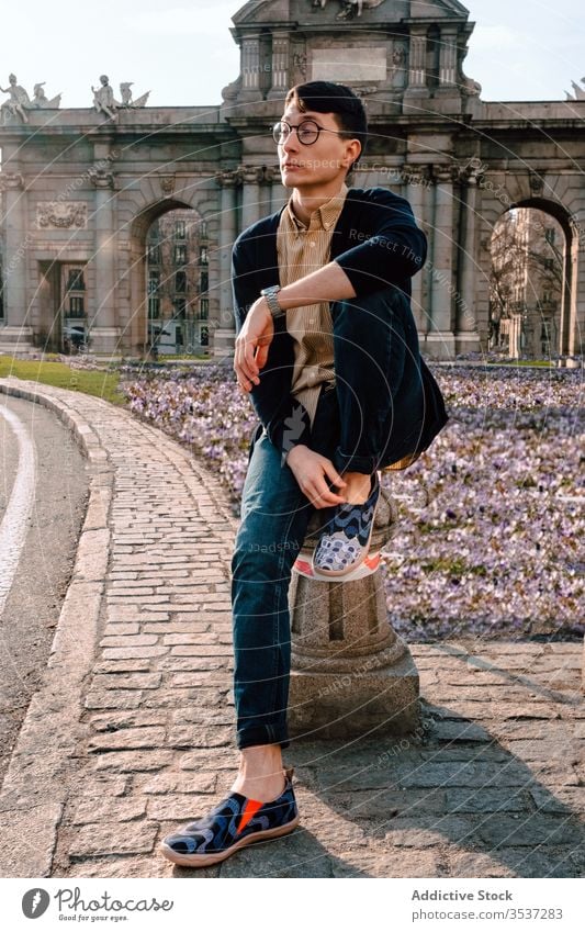 Stylish young Asian man posing in city park trendy style fashion architecture confident exterior asian ancient sight model eyeglasses historic building outfit