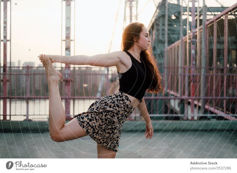 Tranquil woman doing yoga on bridge practice cityscape flexible asana lord of dance pose tranquil female urban scenery casual outfit skirt exercise natarajasana