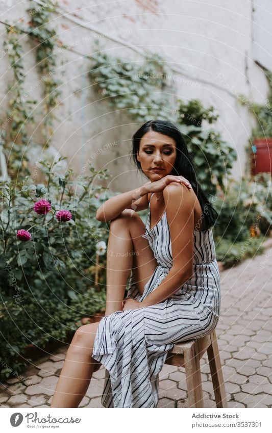 Young woman sitting on stool in garden old pavement style dress barefoot rest female path plant relax serene tranquil peaceful harmony calm summer idyllic flora