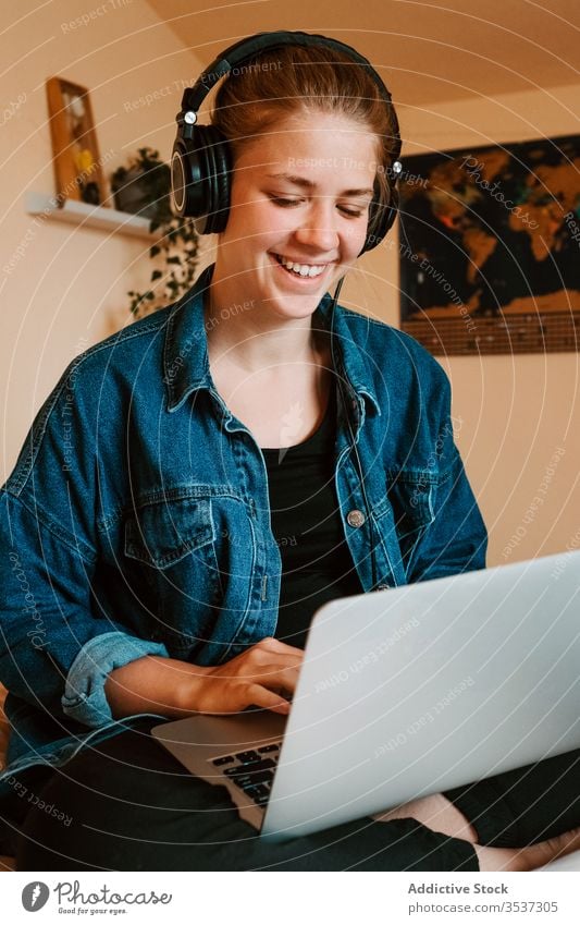 Cheerful young woman using laptop in light bedroom at home headphones read surfing social media watch relax chill listen search lounge check joy rest browsing