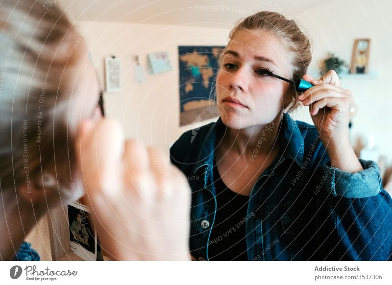 Young woman applying makeup to eyes in light bedroom at home mascara reflection mirror eyelashes make up cosmetic visage brush face female apartment appearance