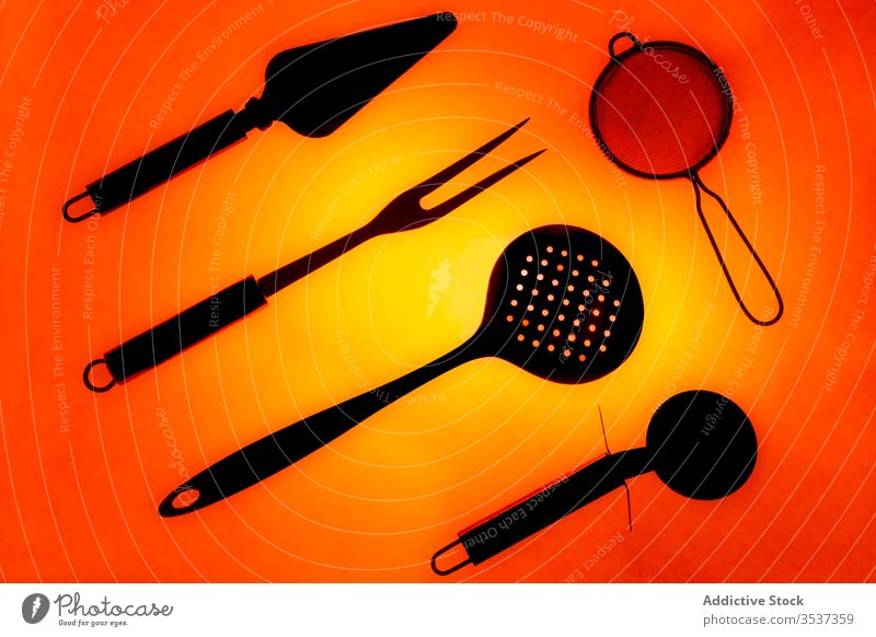 Set of various kitchen utensils on blue background set composition arrangement tool object equipment black illuminate shiny strainer dark light glow collection