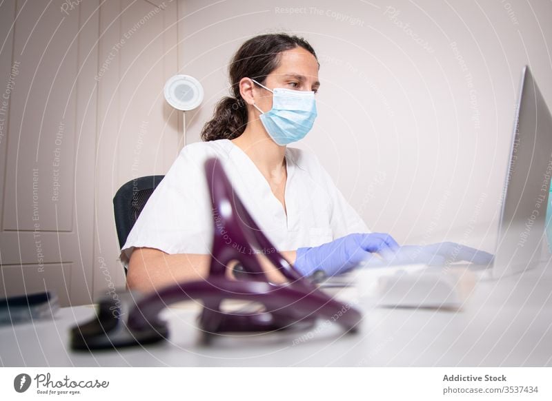 Young female doctor in medical mask working on laptop in clinic woman uniform glove desk serious hospital professional covid 19 coronavirus pandemic outbreak