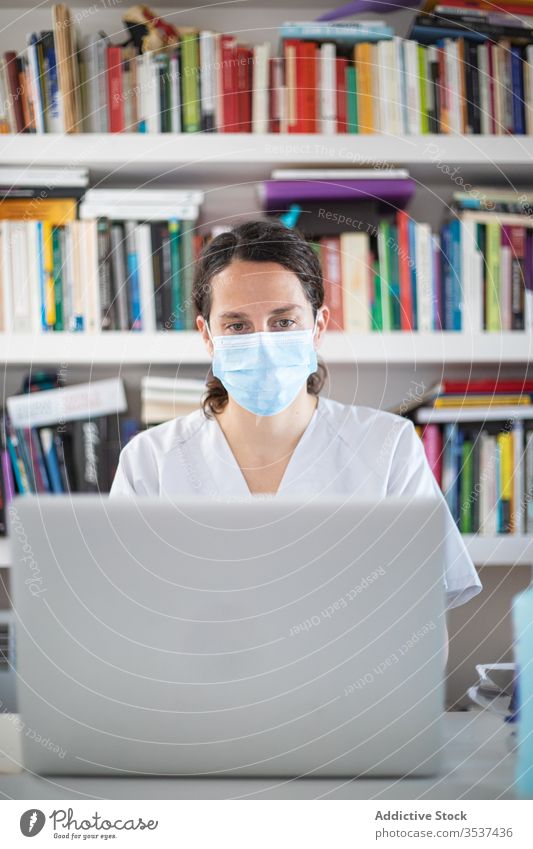 Young female doctor in medical mask working on laptop in clinic woman uniform glove desk serious hospital professional covid 19 coronavirus pandemic outbreak