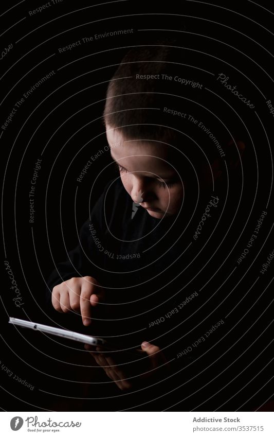 Curious little boy using tablet in studio with black wall curious child serious adorable explore portrait browsing gadget kid childhood digital wireless device