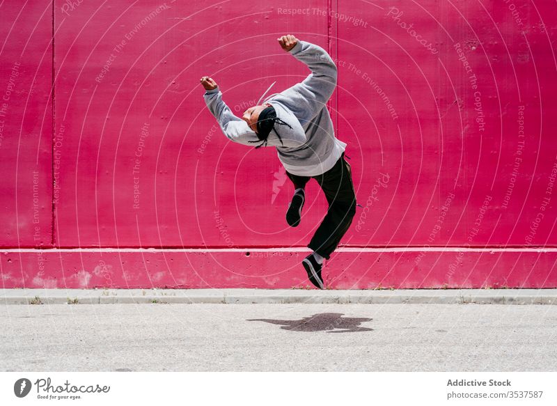 Young hispanic men jumping near to a pink wall on the street urban dance lifestyle city posing standing colorful daylight mixed hat hip-hop cool modern male