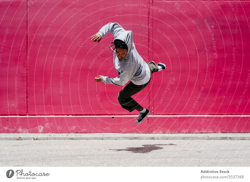 Young hispanic men jumping near to a pink wall on the street urban dance lifestyle city posing standing colorful daylight mixed hat hip-hop cool modern male