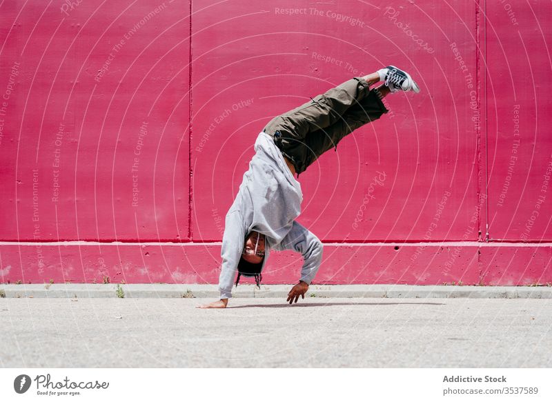 Young hispanic men doing acrobatics near to a pink wall on the street urban dance lifestyle city posing standing colorful daylight mixed hat hip-hop cool modern