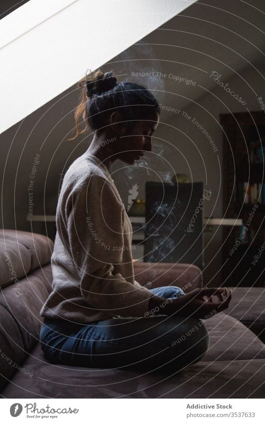 Serene ethnic woman meditating during aromatherapy at home meditate yoga incense sage serene lotus pose pleasant enjoy smell female indian hindu tranquil calm