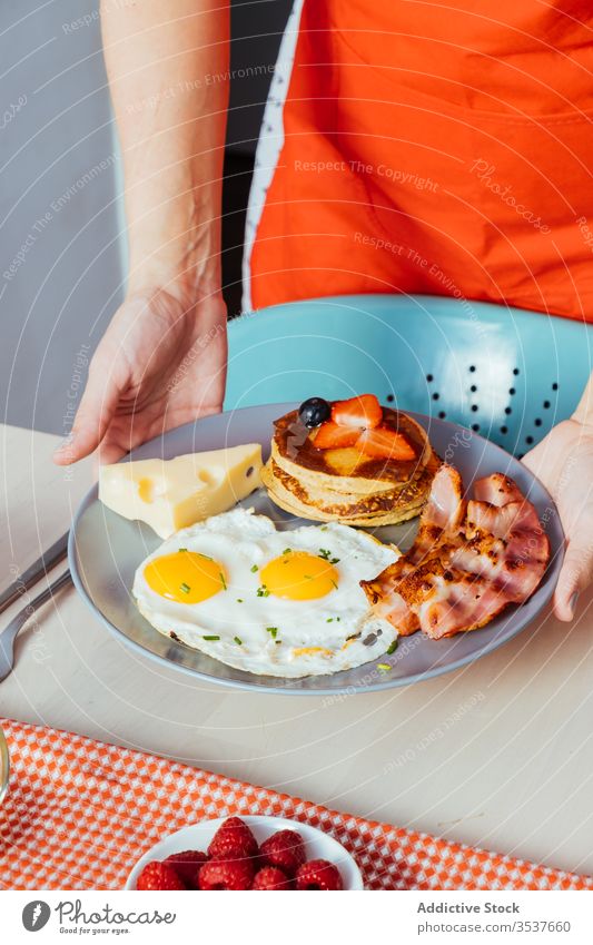 Anonymous crop hands putting plates with raspberry and honey on table for breakfast tasty food morning sweet fresh healthy fruit meal dish yummy snack portion