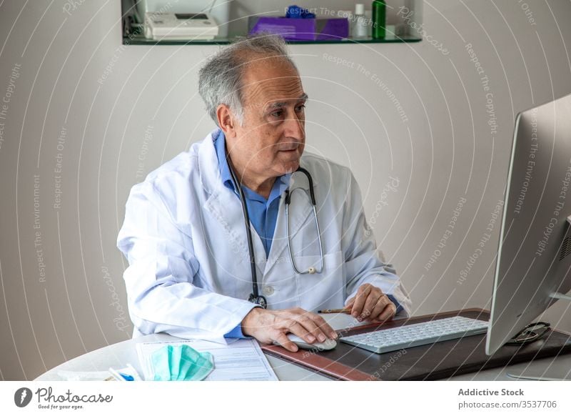 Elderly male physician conducting telemedicine consultation via laptop in clinic man elderly doctor telehealth outbreak using senior aged gray hair medical gown