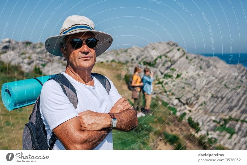 Senior man trekking looking at camera senior mature landscape hike nature countryside hikers summer mountain recreation hat serious sunglasses people hiking