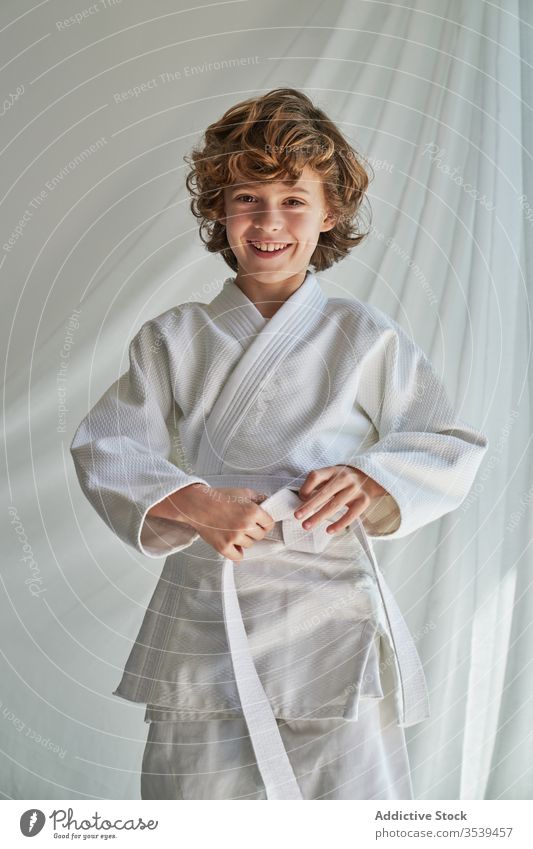 Positive young boy in white kimono practicing judo at home training belt martial studio determine smile confident sport positive childhood joy cheerful