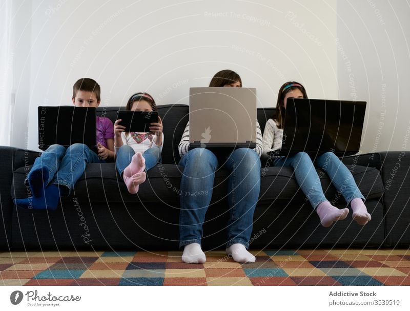 Serious mother and kids spending time together using gadgets on sofa at home children laptop busy addict browsing woman leisure separate sibling parent internet