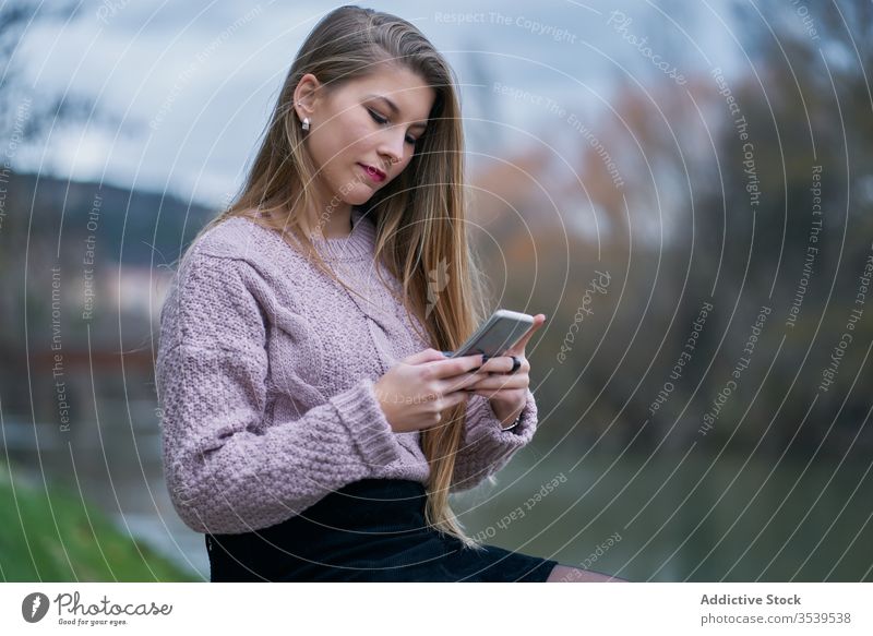 Smiling female browsing smartphone while resting in park at sunset woman happy cheerful glad using watching social media stone bench recline smile internet