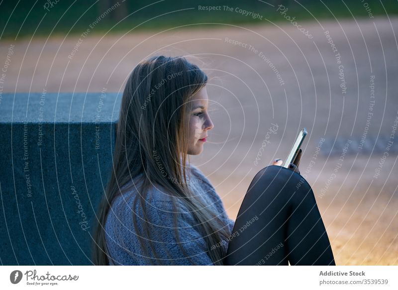 Smiling female browsing smartphone while resting in park at sunset woman happy cheerful glad using watching social media stone bench recline smile internet