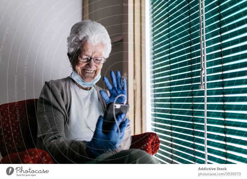 Cheerful senior woman chatting on smartphone during self isolation at home stay coronavirus window using cheerful communicate mobile device gadget smile