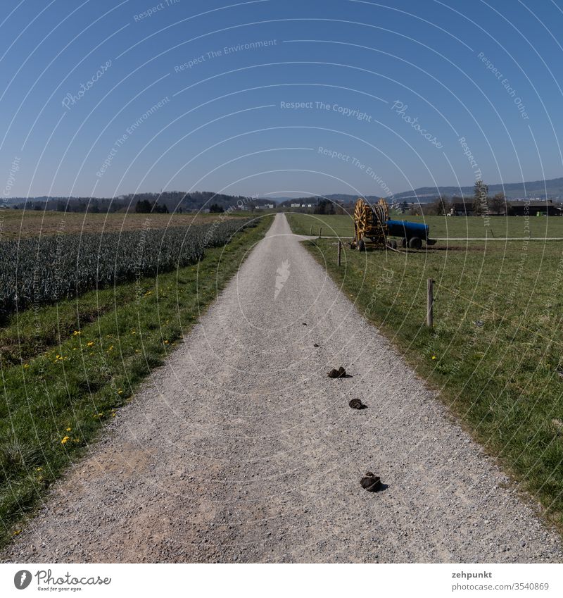 View along a path over farmland, agricultural machinery at the next crossroads, in the background a settlement Agriculture off the beaten track