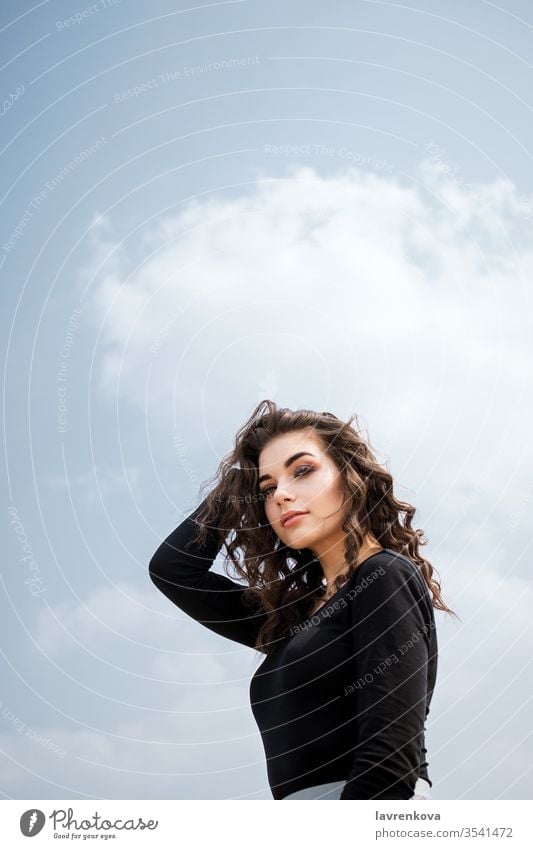 Portrait of young adult white female in front of blue sky, selective focus caucasian freedom curly hair brunette spring alone attractive girl lifestyle make up