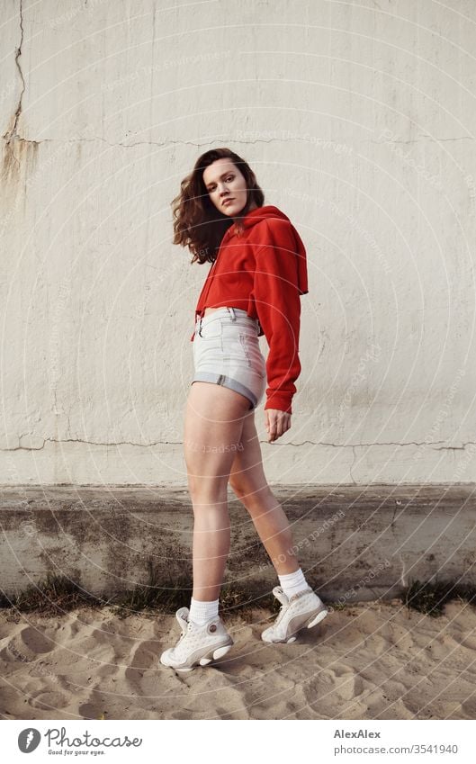 Portrait of a young, laughing woman in the sand in front of a wall Sandy beach Face Shallow depth of field Self-confident Thin Looking into the camera