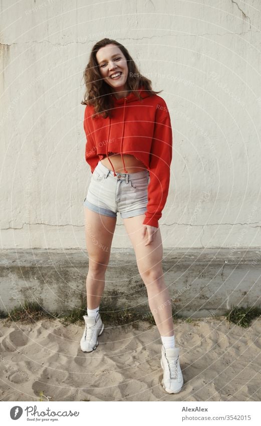 Portrait of a young, laughing woman in the sand in front of a wall Sandy beach Face Shallow depth of field Self-confident Thin Looking into the camera