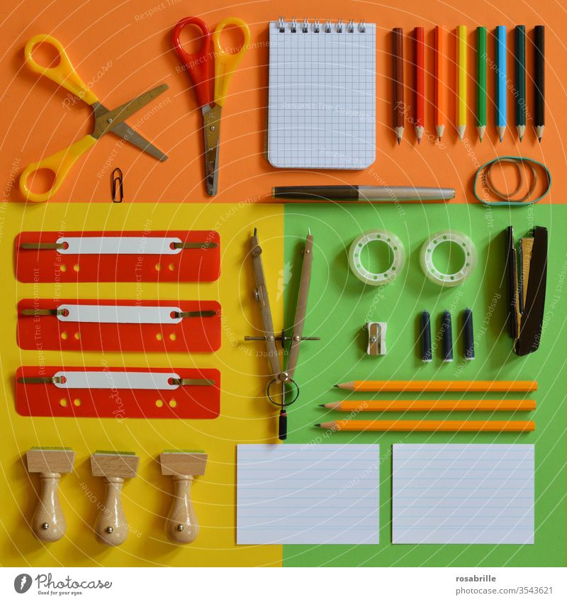 colourful flat lay with office utensils such as scissors stamps compasses ink cartridge fountain pen rubber band coloured pencils pencils quick fasteners paper clip notepad stapler tacker adhesive tape index cards on orange yellow green paper against the dreary everyday working life