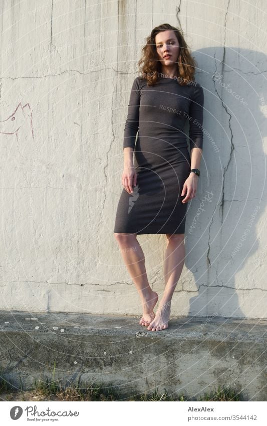 Portrait of a young woman in front of a concrete wall on the beach Woman girl Slim brunette Curl long hairs Evening portrait 18-25 years Youth (Young adults)