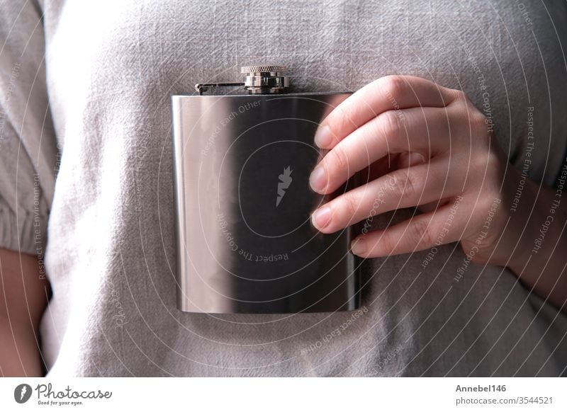 Hand holding a stainless steel flask for liqueur, alcohol and beverage concepts in close-up background alcoholic Drinking Design by hand booze Party Steel Water