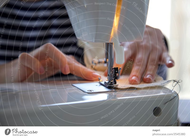 Hands of a young woman push a piece of fabric through the foot of a sewing machine. Sewing Tailoring Sewing machine hands Handcrafts Cloth Stitching threads