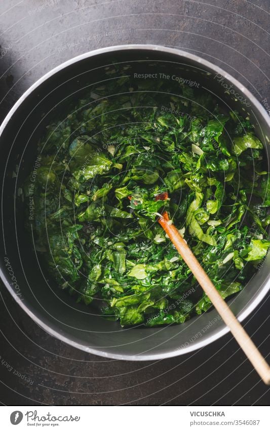 Close up of chopped stewed spinach in cooking pan with wooden spoon on rustic kitchen table. close up top view vegetarian healthy eating concept pot closeup