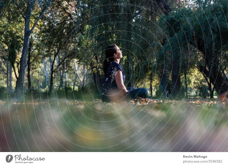 Beautiful woman seated on grass in front of sun doing yoga back balance concentration exercise fit fitness lotus meditate meditating meditation mental peace