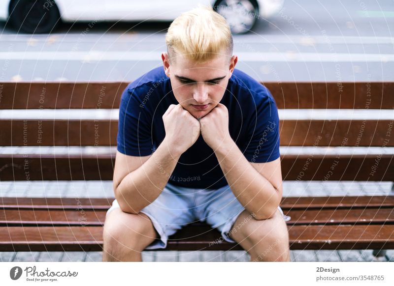 Young boy sitting on a bench in the street with his hands on his face worried and sad man 1 male person young single worry stress park one problem guy sorrowful