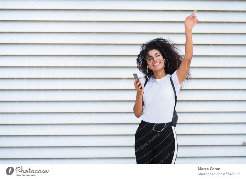 beautiful mixed race girl listening music happy in the street three quarter lenght young white background dancing sunlght woman lifestyle earphones brown hair