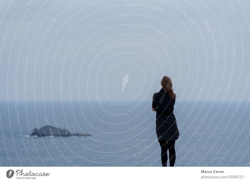 young woman standing against a blue sky and sea thoughtful thinking horizon cold future ethereal uncertainly sadness breeze tranquil scene outdoors calm nature