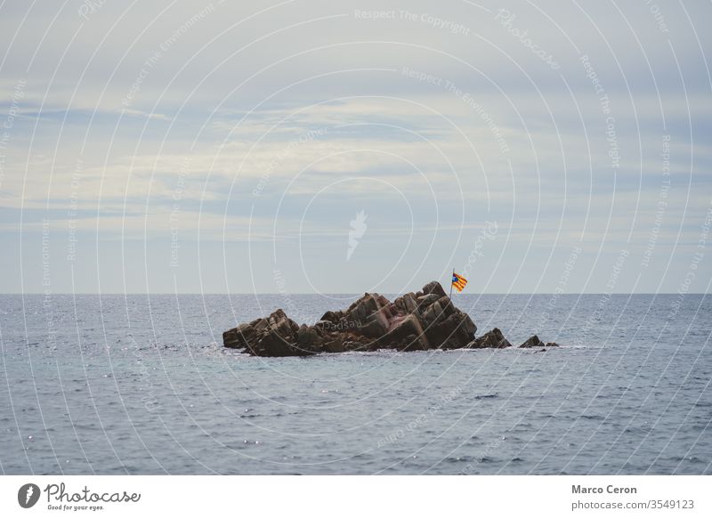 flag flies on a desert islet in the middle of the sea fly nationalist sky water emblem rock symbolic patriotic proud wave nationalism seascape windy icon