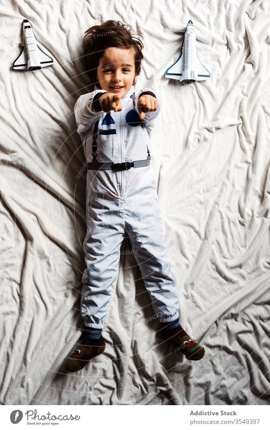 Boy in astronaut costume lying on bed boy spacesuit toy spaceship having fun smile kid cosmonaut bedroom child cheerful weekend rocket playful uniform pretend