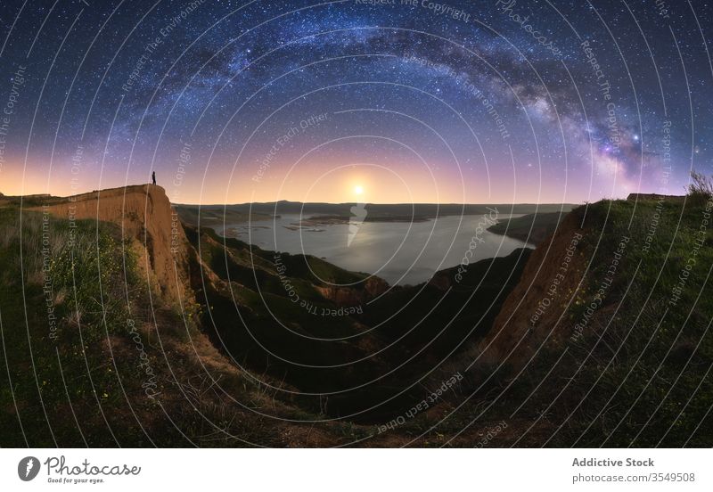 Canyon with anonymous person under colorful nigh sky with milky way canyon nature lake galaxy cloudy silhouette water formation hill landscape rock traveler