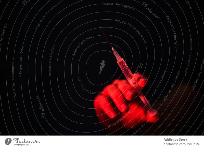 Crop person holding syringe with medication in red light on black background vaccine cure injection hospital clinic covid 19 coronavirus infection disease