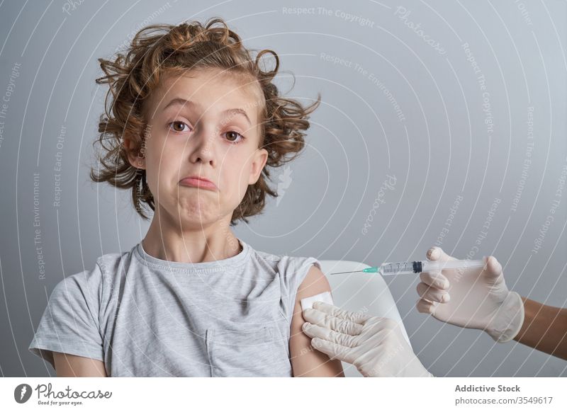 Anonymous doctor holding boy shoulder during injection in clinic vaccine treat syringe medicine glove patient health care procedure work healthy cure kid tool