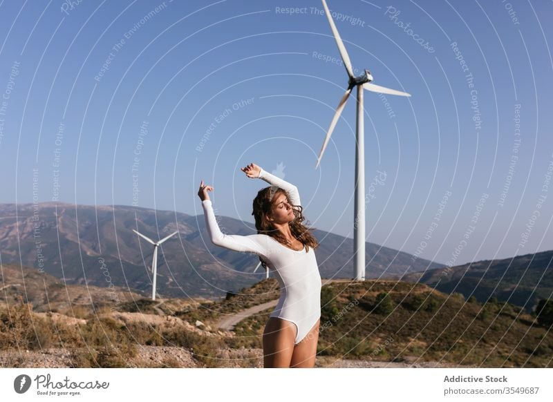 Tender female dancing alone near wind farm on sunny field woman dance countryside sensual nature ecology slim style hand up alternative windmill energy move