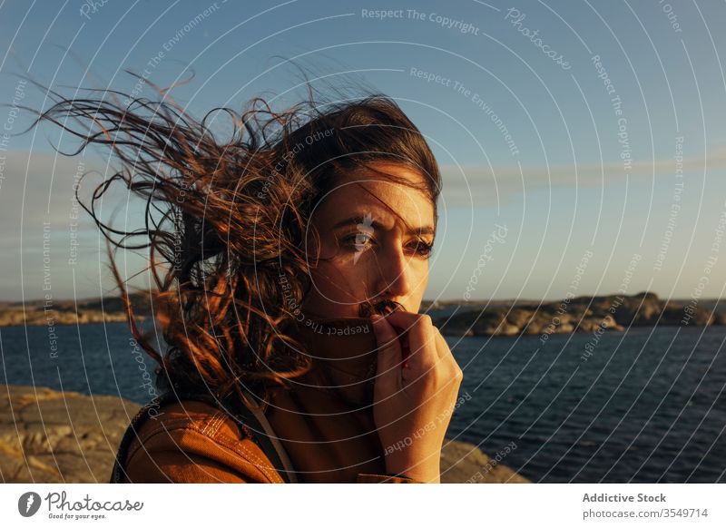 Thoughtful young female tourist standing on rocky seashore and looking away woman traveler harmony dream pensive wave hair wind nature coast vacation thoughtful