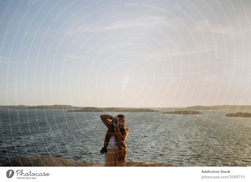 Anonymous female tourist standing on rocky seashore and taking photos woman take photo cliff coastline seascape nature journey photo camera tourism vacation