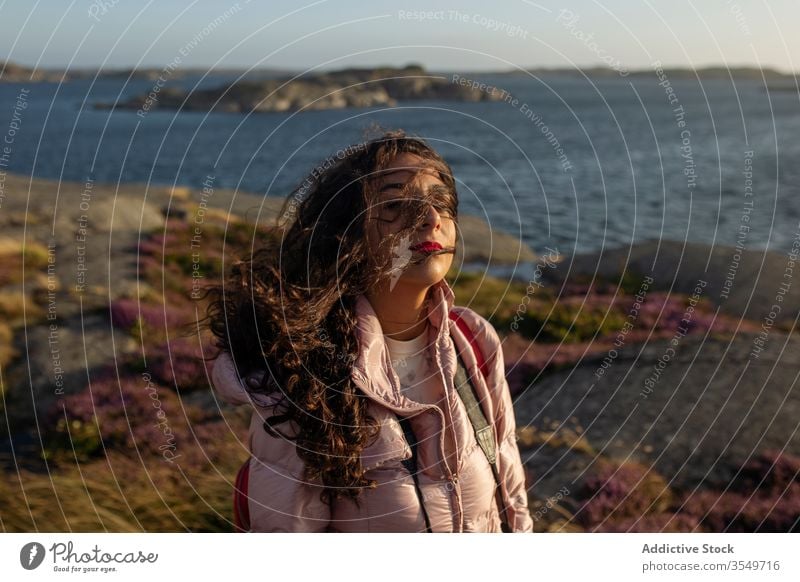 Young woman standing near lake shore breeze enjoy sunny female calm tranquil serene wind wavy hair relax vacation holiday rest water river pensive thoughtful