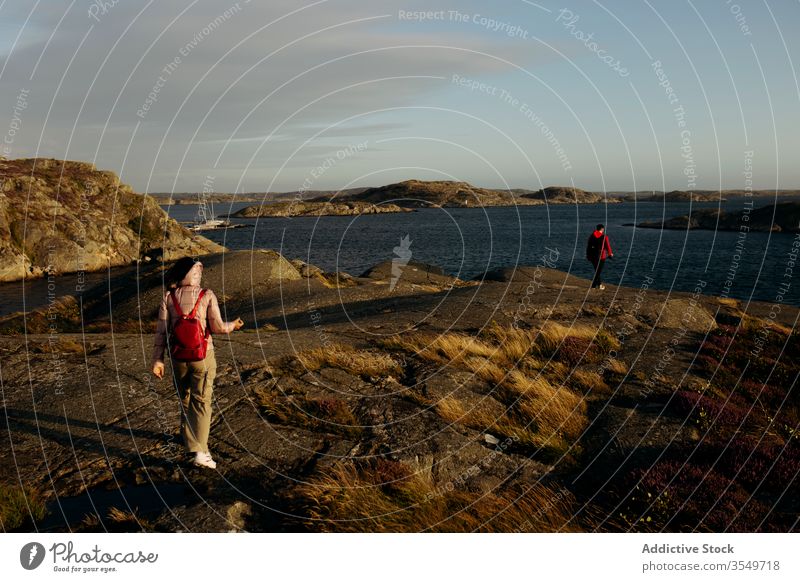 Anonymous couple of tourists walking on rocky seashore together seascape outerwear vacation nature travel adventure tourism relationship journey landscape