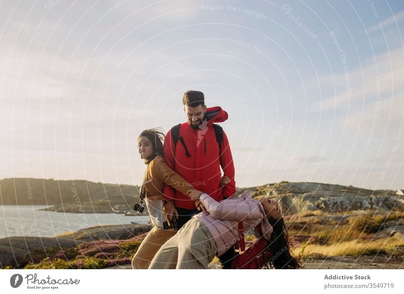 Group of positive young tourists having fun on rocky seashore group together cheerful playful tourism outerwear nature cliff sunny vacation travel journey