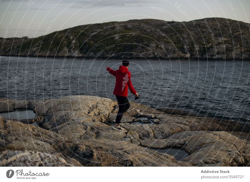 Male tourist with photo camera standing on rocky lake shore man travel contemplate hill lakeside cloudy sky river stone explore vacation tourism weekend casual